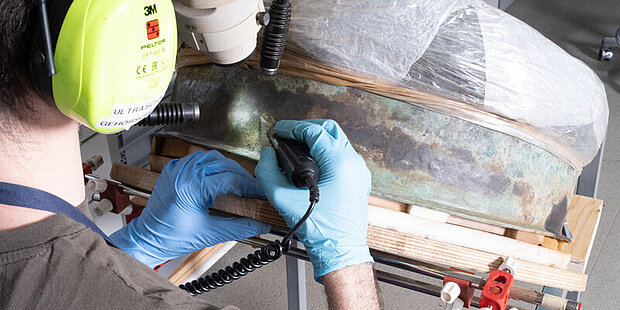 A conservator is sitting at the sandblasting machine with an object